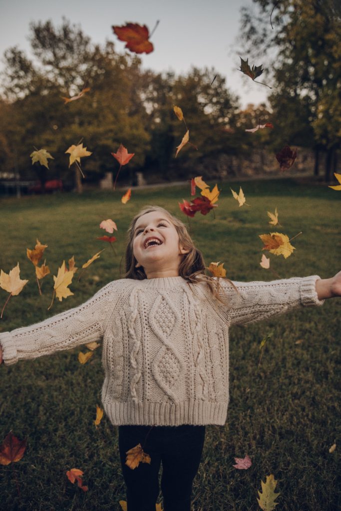Young female child smiling and looking up as fall leaves fall around her. Nurturing mindfulness
