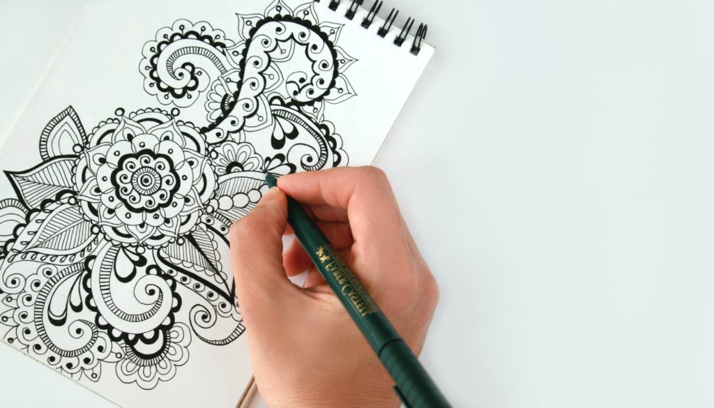 Hand with green pen doodling on a top spiral notebook, engaging in mindful doodling