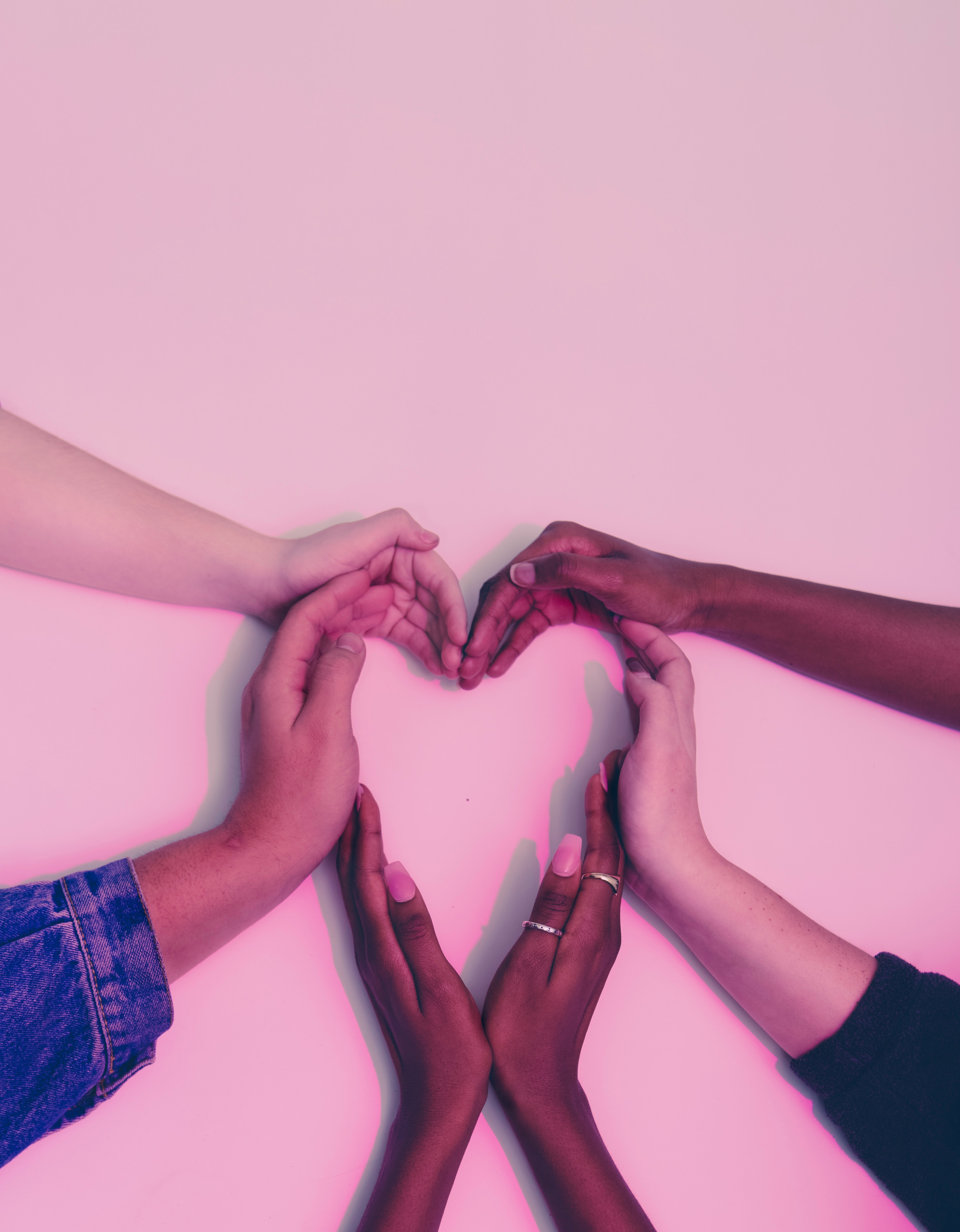 Multiple hands forming a heart on a pink background