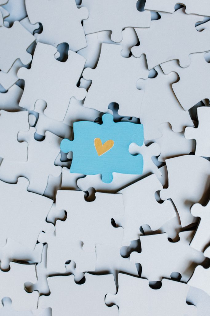 A blue puzzle piece with a gold heart on top of multiple puzzle pieces.