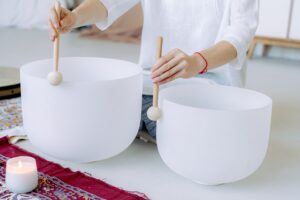 2 different size crystal bowls with a person holding a mallet on the sides of each bowl.