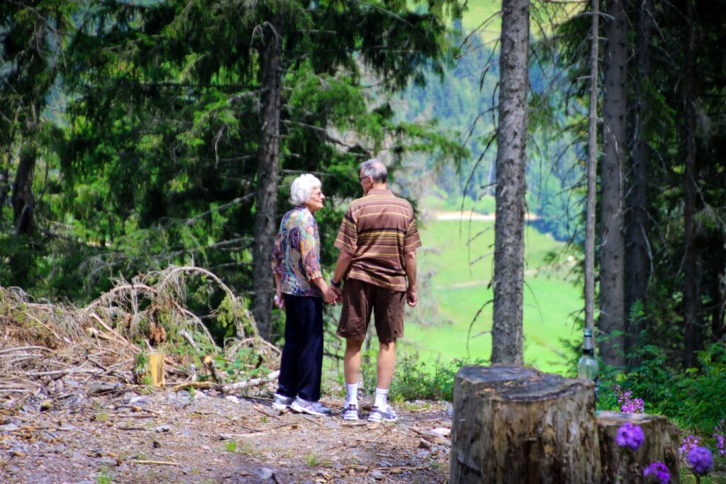 An older couple standing in the woods looking at each other holding hands