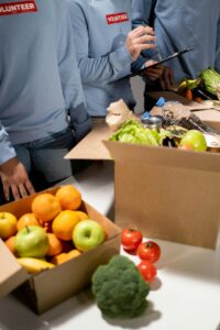 boxes of fruits and vegetables with volunteers standing next to them
