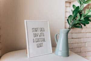 Blue vase with a plant next to a plaque that says "Start each day with a grateful heart"