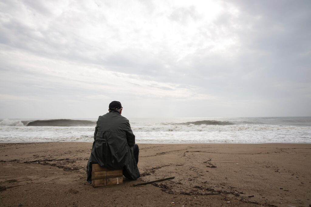 A man sitting on wood blocks at a beach looking at the ocean